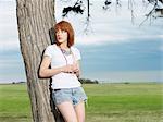 Young woman leaning against tree, Williamstown beach, Melbourne, Australia