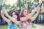 Two young female friends taking selfie on smartphones side by side