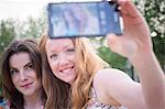 Close up of two young female friends in park taking selfie on smartphone