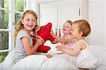 Three girls playing on bed with soft toy