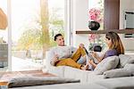 Couple reading newspaper and looking at digital tablet on sitting room sofa