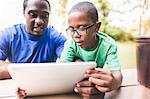 Father looking at digital tablet with son at eco camp
