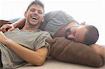 Male couple reclining and laughing on sitting room floor cushions