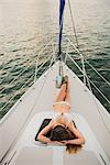 Mid adult woman lying on boat deck wearing bikini