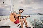 Young man on sailing boat playing guitar