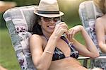 Mature woman wearing bikini, relaxing on sun lounger, drinking wine