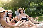 Three mature women relaxing in sun loungers, drinking wine