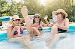 Three mature women sitting in paddling pool, drinking wine