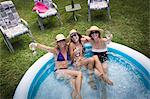 Three mature women sitting in paddling pool, drinking wine, elevated view