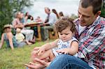 Father playing with daughter at family gathering, outdoors