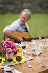 Table with half finished drinks, mature man playing guitar in background