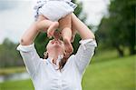 Mid adult woman holding baby girl in air, outdoors
