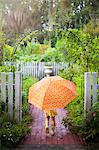Girl walking through garden gate carrying umbrella