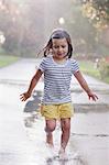 Barefoot girl running through puddles on rainy street