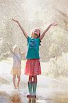 Two girls with arms open standing in water spray on street