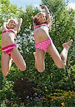 Girls in swimming costume jumping in garden