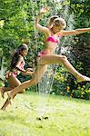 Girls in swimming costume jumping over garden sprinkler