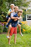 Three boys playing piggyback in garden