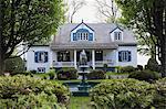 White with blue trim 1920s cottage style house facade with water fountain, Quebec, Canada