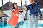 Little boy having fun with his parents by swimming pool