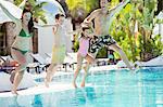 Parents with son and daughter holding hands, jumping into swimming pool