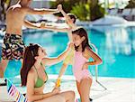 Mother applying suntan lotion on daughter's face by swimming pool