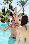 Father giving piggyback ride to his two children in swimming pool