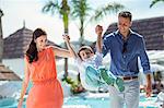 Boy holding hands with his parents by swimming pool