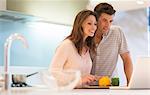 Smiling couple cutting bell peppers and looking at laptop in modern kitchen