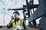 Worker using walkie-talkie near crane