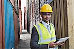 Businessman holding digital tablet between cargo containers