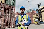 Worker holding clipboard near cargo containers