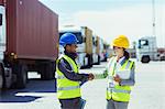 Worker and businesswoman shaking hands near trucks and cargo containers