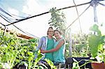 Portrait of smiling couple embracing in greenhouse, seedlings in foreground