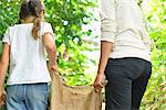 Rear view of woman and girl carrying burlap sack through garden