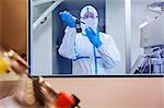 Scientist in clean suit pipetting sample into Petri dish in laboratory