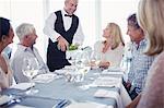 People sitting at restaurant table, waiter pouring white wine