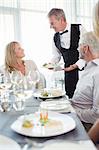 Waiter serving fancy dish to woman sitting at restaurant table