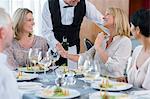 Waiter offering wine to female client at restaurant table, woman refusing