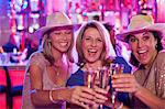 Portrait of three cheerful women wearing cowboy hats toasting with champagne flutes in nightclub