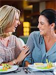 Two female friends talking and laughing in restaurant, fancy dishes on table