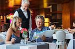 Man ordering meal at fancy restaurant table, waiter standing behind