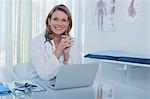 Portrait of smiling female doctor sitting at desk with laptop