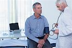 Mature doctor taking patient's blood pressure in office