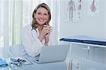 Portrait of smiling female doctor sitting at desk with laptop in office