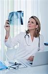Female doctor looking at x-ray at desk with laptop in office