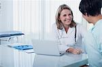 Smiling female doctor and woman sitting at desk in office