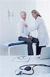 Blood pressure gauge, laptop, file and glasses on desk in doctor's office, female doctor examining patient in background