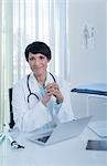 Portrait of smiling female doctor sitting at desk with laptop in office