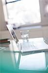 Open laptop and glass of water on glass desk in office